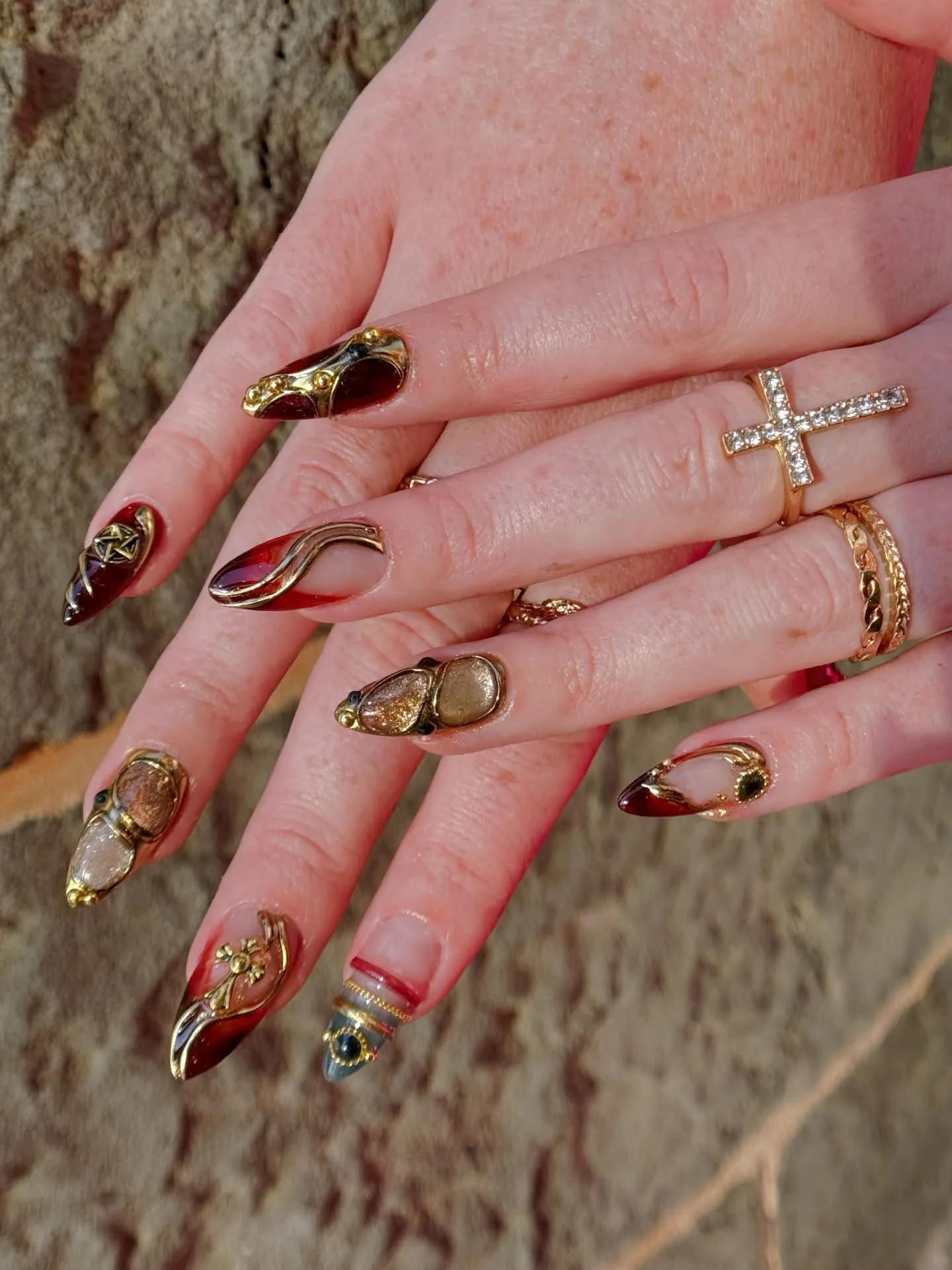 Baroque red and gold nail art with gem insets, both hands in sunlight