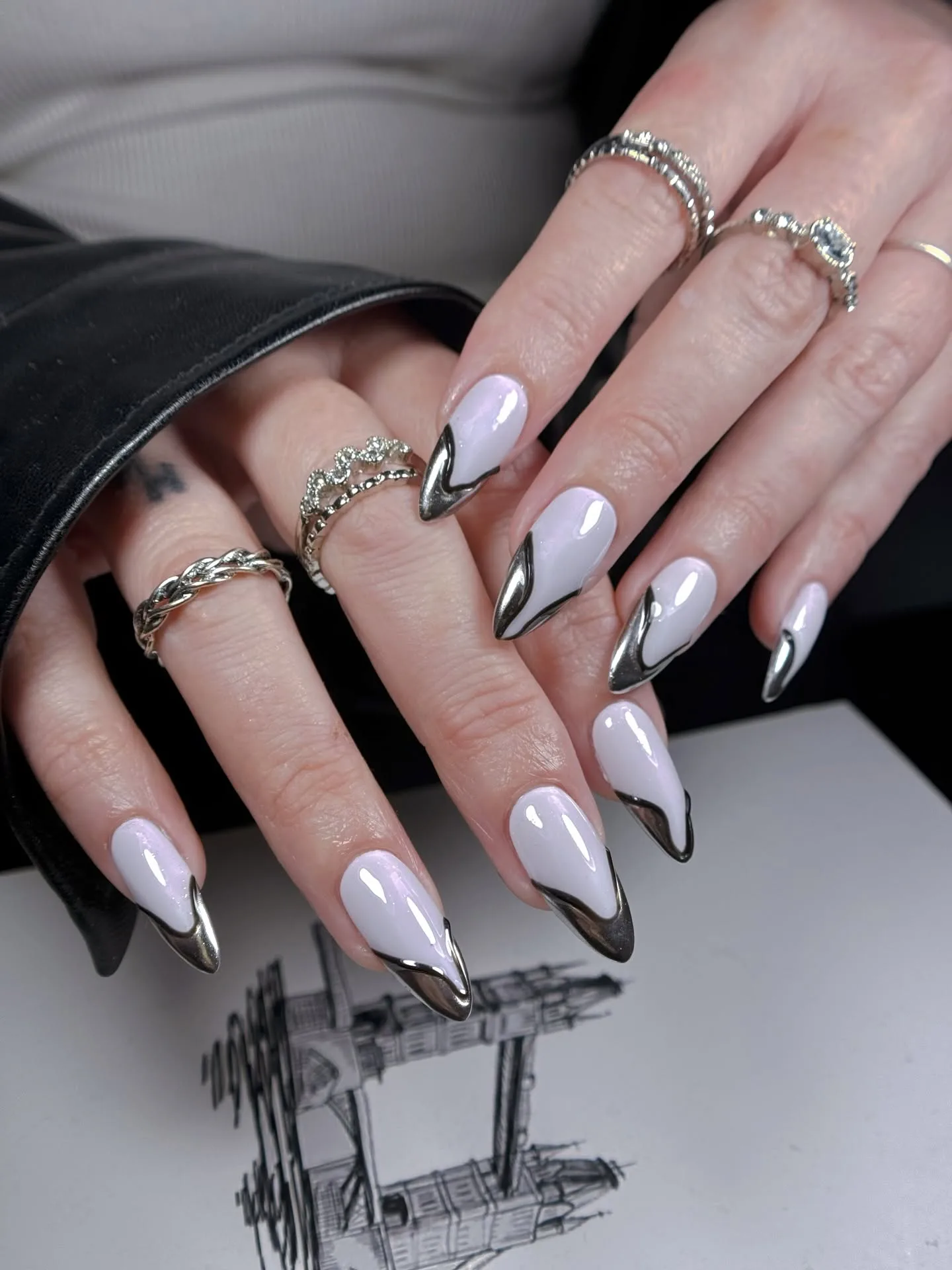 Milky-white nails with liquid silver-chrome French tips and stacked silver rings